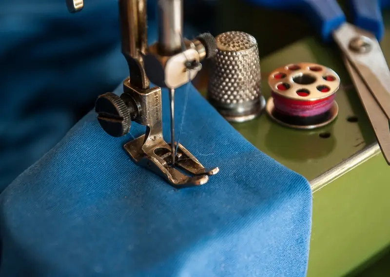 A sewing machine needle stitching through blue denim